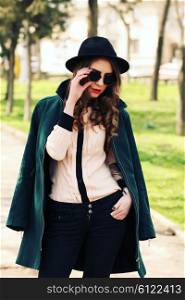 Pretty young fashion smiling blonde woman in sunglasses and vintage hat with leather bag posing outdoor in green park background in spring sunny weather. Fashion image of stylish hipster girl