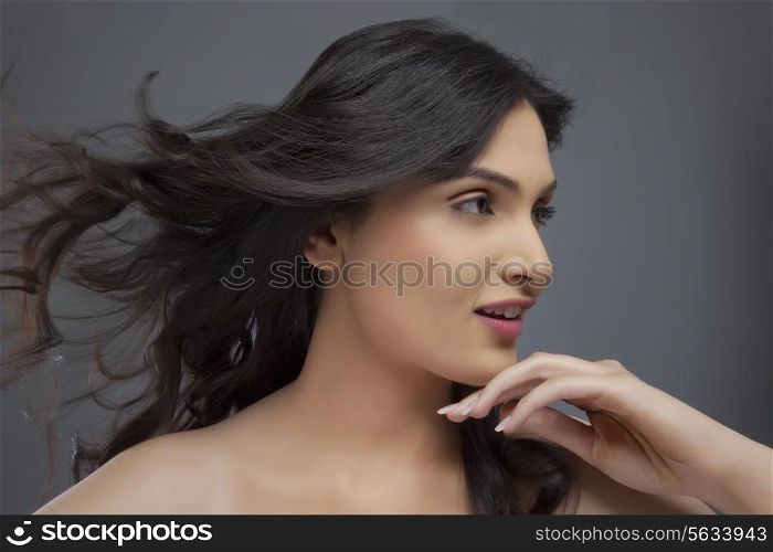 Pretty young female looking away with hair blowing over colored background