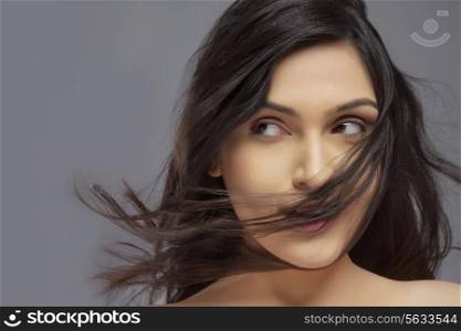 Pretty young female with hair blowing over face against colored background