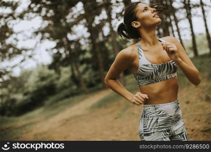 Pretty young fitness woman running at the forest trail