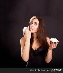 Pretty young girl eating cake on dark background