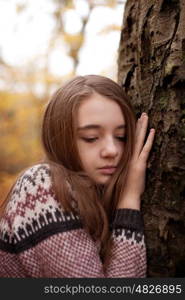 Pretty young girl leaning hand against a tree looking sad