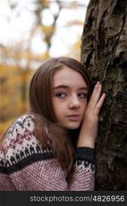 Pretty young girl leaning hand against a tree looking worried