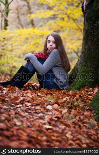 Pretty young girl sitting on dried leaves in a forrest in Autumn