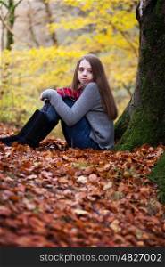 Pretty young girl sitting on dried leaves in a forrest in Autumn