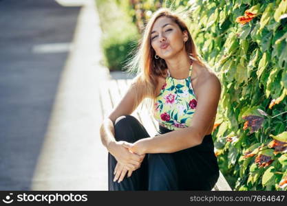 Pretty young girl sitting on urban bench blowing a kiss outdoors. Pretty young girl sitting on urban bench blowing a kiss