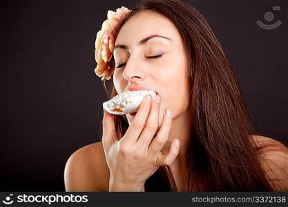 Pretty young girl with closed eyes eating cake on dark background