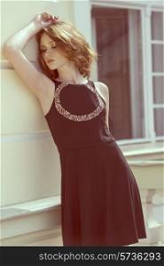 pretty young girl with natural hair-style and stylish black dress posing in outdoor fashion shoot near building