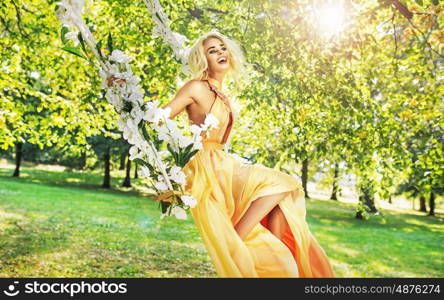 Pretty young lady swinging in the middle of the garden