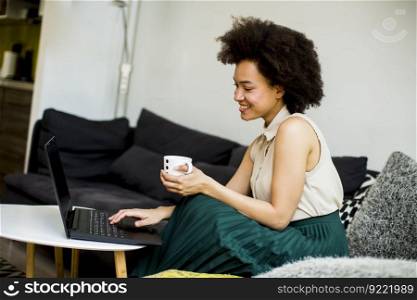 Pretty young lady with curly hair work on the notebook while sit down on the couch at home