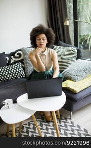 Pretty young lady with curly hair work on the notebook while sit down on the couch at home