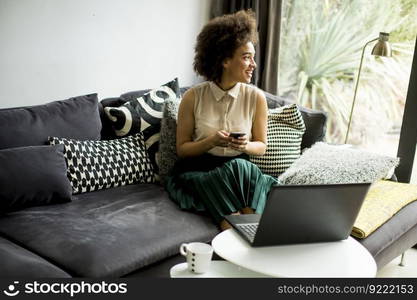 Pretty young lady with curly hair work on the notebook while sit down on the couch at home