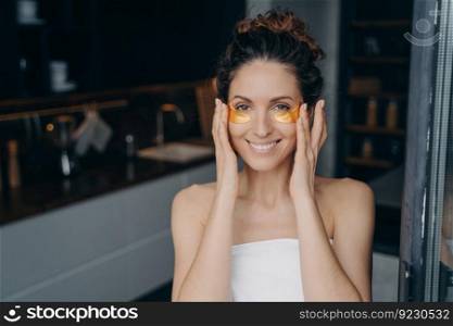 Pretty young lady wrapped in towel after bathing is happy and relaxing at home or hotel room. European girl applying eye patches. Spa resort, body care. Having rest on weekend or vacation concept.. Pretty young lady wrapped in towel after bathing is happy and relaxing applying eye patches.