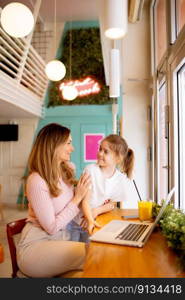 Pretty young mother and her daughter working on laptop and drinking fresh orange juice in the cafe