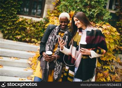 Pretty young multiethnic friends walking with coffee cups on autumn day