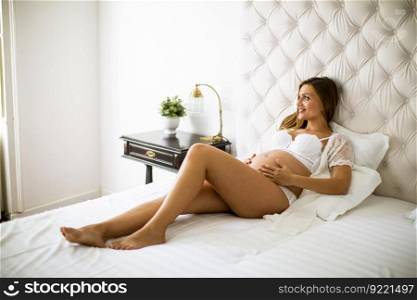Pretty young pregnant woman lying on the bed in room