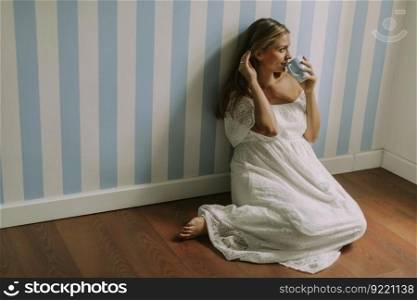 Pretty young pregnant woman sitting on a floor by the wall in the room