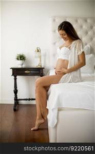 Pretty young pregnant woman sitting on the bed