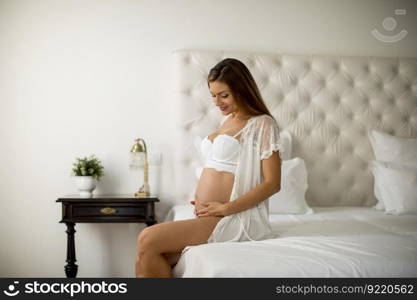 Pretty young pregnant woman sitting on the bed