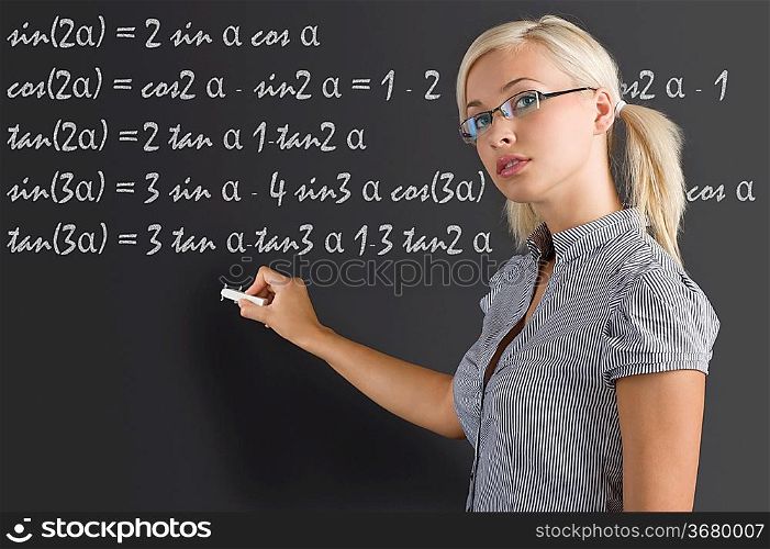 pretty young teacher with blond hair and glasses taking a math lesson on the blackboard