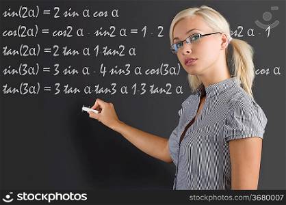 pretty young teacher with blond hair and glasses taking a math lesson on the blackboard