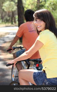 Pretty young woman and her boyfriend riding bikes through the woods