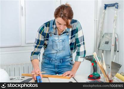 pretty young woman builder measuring a plank of wood