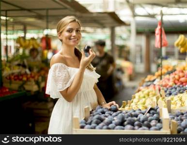 Pretty young woman buying fresh plums on the market