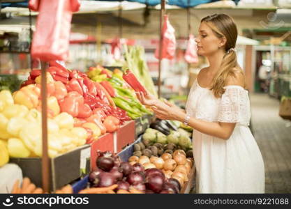 Pretty young woman buying fresh vegetables on the market