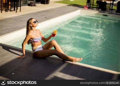 Pretty young woman by the swimming pool with cocktail