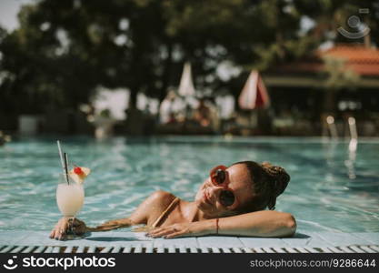 Pretty young woman by the swimming pool with cocktail