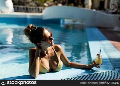 Pretty young woman by the swimming pool with cocktail