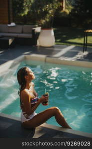 Pretty young woman by the swimming pool with coctail