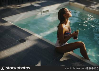 Pretty young woman by the swimming pool with coctail
