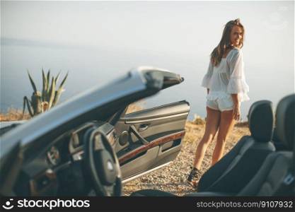 Pretty young woman by the white cabriolet car on the seaside