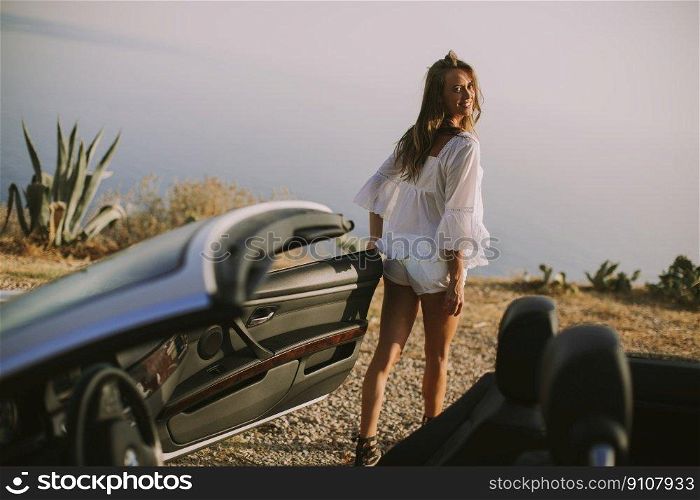 Pretty young woman by the white cabriolet car on the seaside