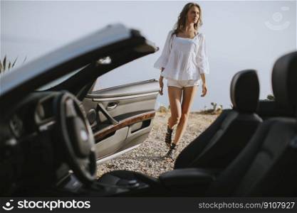 Pretty young woman by the white cabriolet car on the seaside at summer
