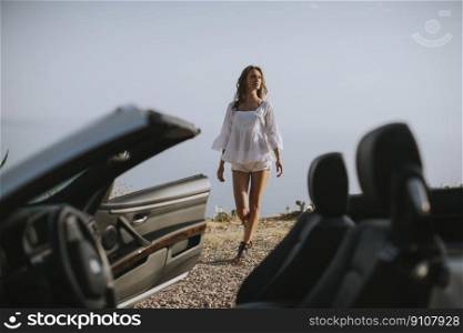 Pretty young woman by the white cabriolet car on the seaside at summer
