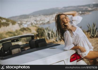 Pretty young woman by white cabriolet car at seaside on a sunny summer day