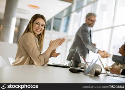 Pretty young woman clapping hands after successful business meeting in the modern office