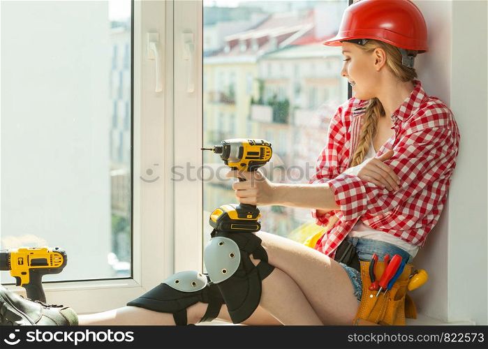 Pretty young woman construction worker with helmet about to fix window picking best tools. Working at flat remodeling. Building, repair and renovation.. Woman with helmet next to the window