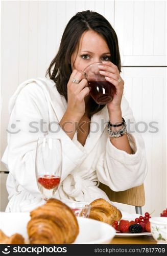 Pretty young woman, dressed in a bathrobe, drinking a cup of tea with both hands on a luxurious sunday morning breakfast