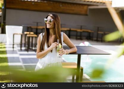 Pretty young woman drinking by the swimming pool on a sunny summer day