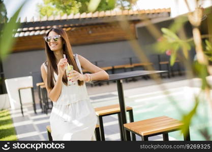 Pretty young woman drinking by the swimming pool on a sunny summer day