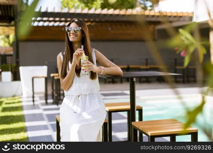 Pretty young woman drinking by the swimming pool on a sunny summer day