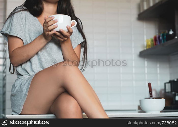 Pretty young woman drinking coffee in kitchen at home