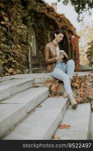Pretty young woman drinking takeaway coffee at the outdoor stairs on autumn day