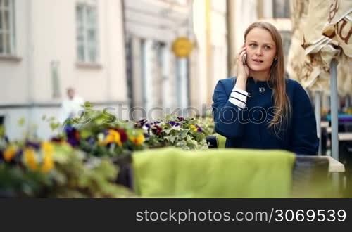 Pretty young woman having a phone talk in outdoor cafe terrace decorated with flowers