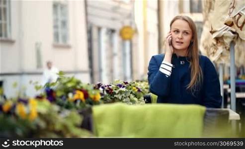 Pretty young woman having a phone talk in outdoor cafe terrace decorated with flowers
