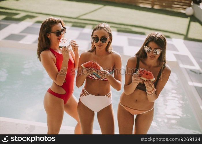 Pretty young woman having fun and eating watermelon by the pool at hot summer day